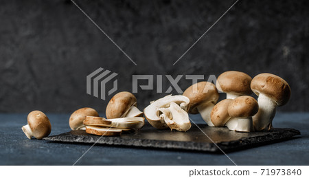 Fresh champignon mushroom slices and whole mushrooms on the granite plate. Fresh champignon mushroom slices and whole mushrooms on the granite plate. 71973840