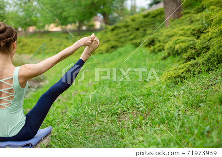 Slender young brunette yoga performs challenging yoga exercises on green grass against a background of nature Slender young brunette yoga performs challenging yoga exercises on green grass against a background of nature 71973939