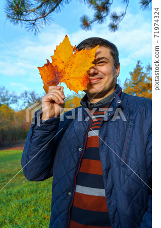 portrait of a man posing in autumn park, covering his face with maple leaf, bright colorful leaves as background portrait of a man posing in autumn park, covering his face with maple leaf, bright colorful leaves as background 71974324