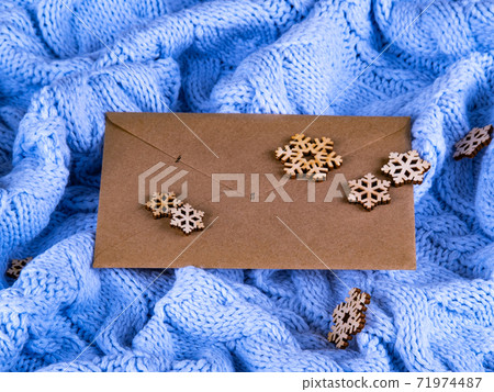 The envelope on the blue wool knitted background with the wooden snowflakes. 71974487