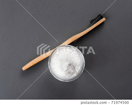 A bamboo toothbrush with toothpowder in a glass on the grey background. A bamboo toothbrush with toothpowder in a glass on the grey background. 71974500