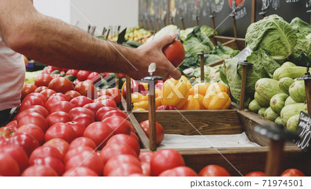 Close-up hands of grocery worker is arranging vegetables on store shelves 71974501