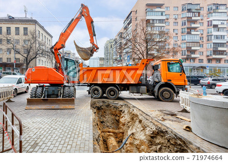An excavator and a truck at the repair of a heating main on a city street. 71974664