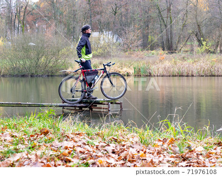Cyclist stay at his trekking bike on small pond pier and watching swans Cyclist stay at his trekking bike on small pond pier and watching swans 71976108