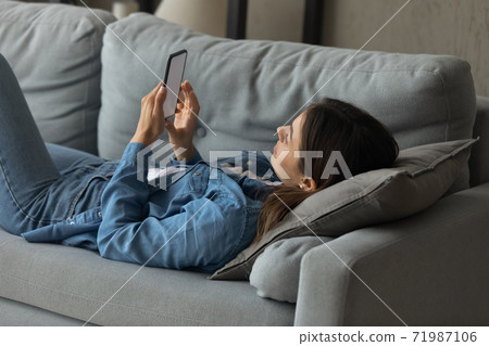 Young woman relax on couch using smartphone Young woman relax on couch using smartphone 71987106