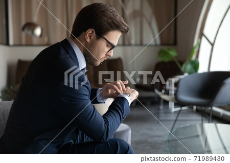 Male employee looking at wristwatch waiting for job interview time Male employee looking at wristwatch waiting for job interview time 71989480