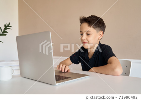 Schoolboy boy sitting at a desk with a laptop, writes school lessons during homework. 71990492