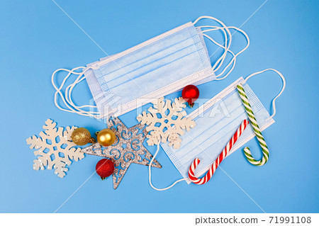 Blue protective medical masks, christmas or new year decor and striped candy cane on a blue background. Top view. Blue protective medical masks, christmas or new year decor and striped candy cane on a blue background. Top view. 71991108
