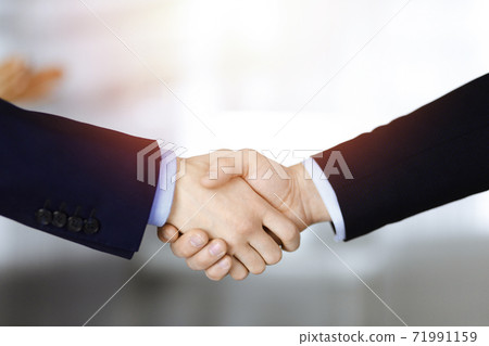 Business people shaking hands at meeting or negotiation, close-up. Group of unknown businessmen and a woman stand together in a sunny modern office. Teamwork, partnership and handshake concept Business people shaking hands at meeting or negotiation, close-up. Group of unknown businessmen and a woman stand together in a sunny modern office. Teamwork, partnership and handshake concept 71991159