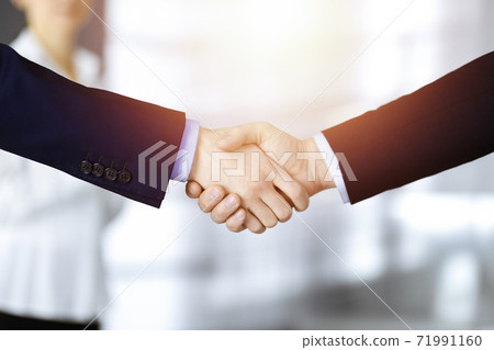 Business people shaking hands at meeting or negotiation, close-up. Group of unknown businessmen and a woman stand together in a sunny modern office. Teamwork, partnership and handshake concept Business people shaking hands at meeting or negotiation, close-up. Group of unknown businessmen and a woman stand together in a sunny modern office. Teamwork, partnership and handshake concept 71991160