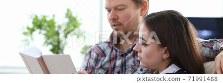 Couple sitting at home and reading book together Couple sitting at home and reading book together 71991488