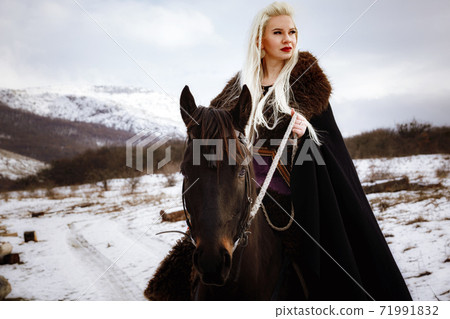Woman viking with a black horse against the background of mountains 71991832