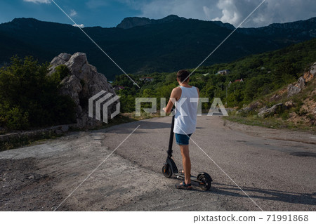 Young man riding an electric scooter on mountain range. 71991868