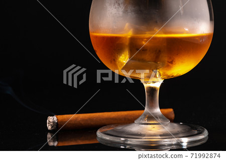 Glass of whisky and lighted cigar on black background 71992874