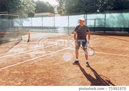 Middle-aged man playing tennis on outdoor tennis filed 71992878