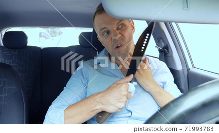 Young handsome man shaving with knife while sitting in car in parking 71993783