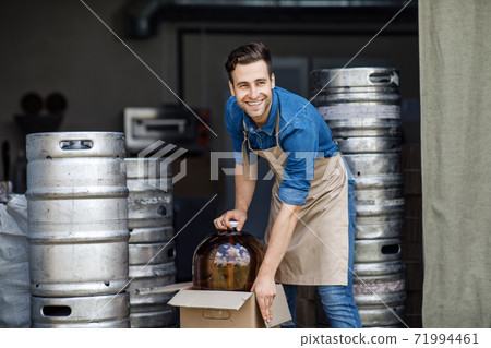 Smiling handsome strong millennial worker guy in apron pulls out big can with ingredients 71994461