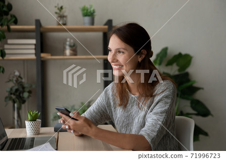 Dreamy young woman looking in distance holding smartphone in hands. 71996723