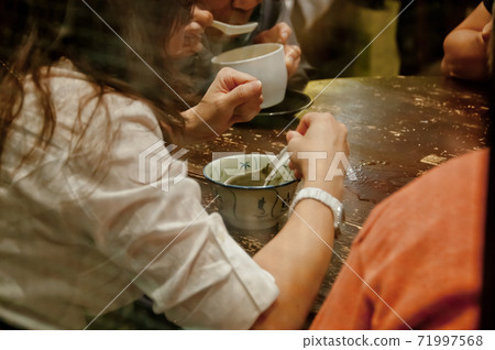 Lady sits and eats famous hot and cold sweet dessert soup in a round table with her friend in Hong Kong restaurant cafe 71997568