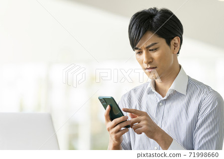 A young man operating a smartphone 71998660