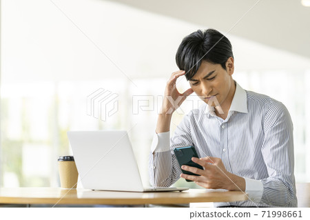 A young man holding his head while looking at the screen of a smartphone 71998661