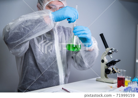 Scientist shaking green fluid in beaker. Young laboratory assistant making test or research in lab. Technician testing chemistry lab experiment and shaking glass tube flask along with microscope Scientist shaking green fluid in beaker. Young laboratory assistant making test or research in lab. Technician testing chemistry lab experiment and shaking glass tube flask along with microscope 71999159