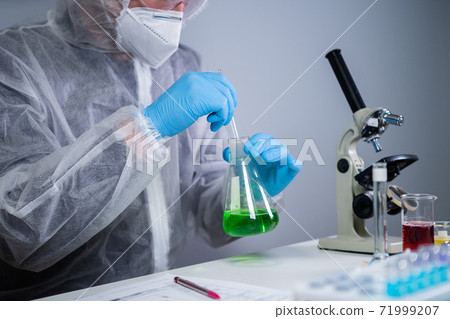 Scientist shaking green fluid in beaker. Young laboratory assistant making test or research in lab. Technician testing chemistry lab experiment and shaking glass tube flask along with microscope Scientist shaking green fluid in beaker. Young laboratory assistant making test or research in lab. Technician testing chemistry lab experiment and shaking glass tube flask along with microscope 71999207