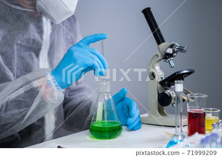Scientist shakes green biochemical product in erlenmeyer flask mixing and research in laboratory. Lab assistant work in corona virus pandemic laboratory, COVID 19. Drug development, medical research Scientist shakes green biochemical product in erlenmeyer flask mixing and research in laboratory. Lab assistant work in corona virus pandemic laboratory, COVID 19. Drug development, medical research 71999209