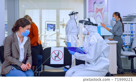 Dentist assistant with ppe equipment talking with patient Dentist assistant with ppe equipment talking with patient 71999221