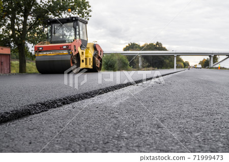 Asphalt road roller with heavy vibration roller compactor press new hot asphalt on the roadway on a road construction site. Heavy Vibration roller at asphalt pavement working. Repairing. 71999473