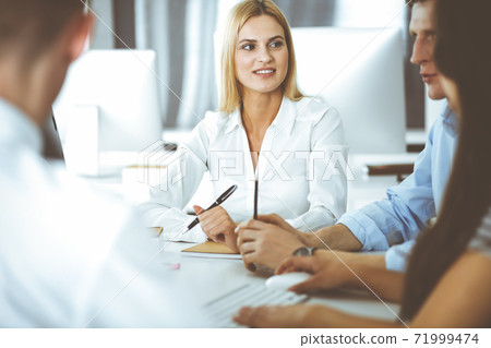 Group of business people discussing questions at meeting. Headshot of blonde businesswoman while smiling to her colleague at office negotiation. Teamwork and cooperation in corporate occupation 71999474