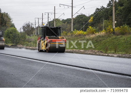 Asphalt road roller with heavy vibration roller compactor press new hot asphalt on the roadway on a road construction site. Heavy Vibration roller at asphalt pavement working. Repairing. Asphalt road roller with heavy vibration roller compactor press new hot asphalt on the roadway on a road construction site. Heavy Vibration roller at asphalt pavement working. Repairing. 71999478