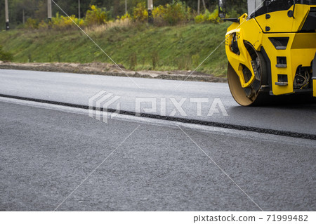 Asphalt road roller with heavy vibration roller compactor press new hot asphalt on the roadway on a road construction site. Heavy Vibration roller at asphalt pavement working. Repairing. Asphalt road roller with heavy vibration roller compactor press new hot asphalt on the roadway on a road construction site. Heavy Vibration roller at asphalt pavement working. Repairing. 71999482