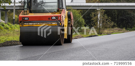 Asphalt road roller with heavy vibration roller compactor press new hot asphalt on the roadway on a road construction site. Heavy Vibration roller at asphalt pavement working. Repairing. Asphalt road roller with heavy vibration roller compactor press new hot asphalt on the roadway on a road construction site. Heavy Vibration roller at asphalt pavement working. Repairing. 71999556