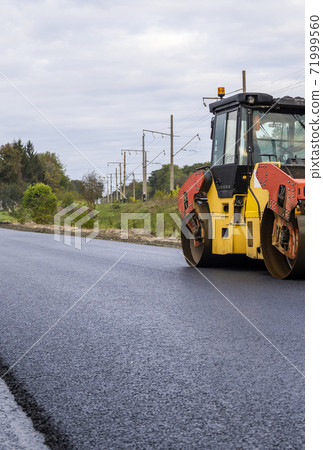 Asphalt road roller with heavy vibration roller compactor press new hot asphalt on the roadway on a road construction site. Heavy Vibration roller at asphalt pavement working. Repairing. Asphalt road roller with heavy vibration roller compactor press new hot asphalt on the roadway on a road construction site. Heavy Vibration roller at asphalt pavement working. Repairing. 71999560