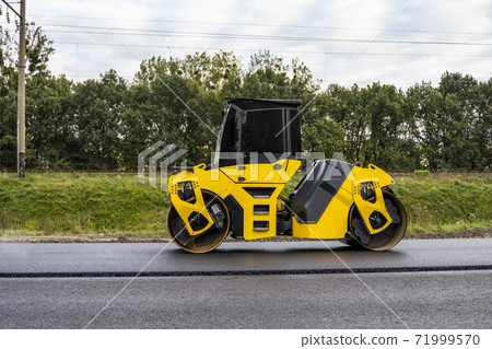 Asphalt road roller with heavy vibration roller compactor press new hot asphalt on the roadway on a road construction site. Heavy Vibration roller at asphalt pavement working. Repairing. Asphalt road roller with heavy vibration roller compactor press new hot asphalt on the roadway on a road construction site. Heavy Vibration roller at asphalt pavement working. Repairing. 71999570