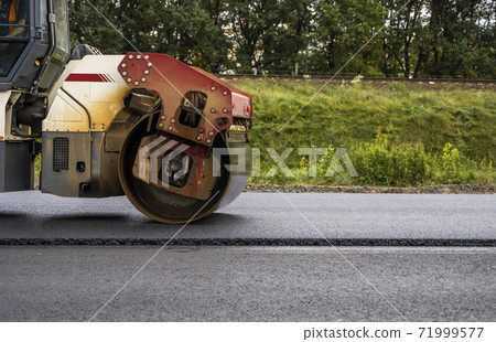 Asphalt road roller with heavy vibration roller compactor press new hot asphalt on the roadway on a road construction site. Heavy Vibration roller at asphalt pavement working. Repairing. 71999577