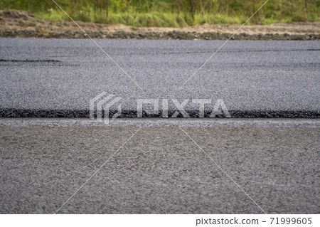 A large layer of fresh hot asphalt. Layer of asphalt raw material in a shallow depth of field. Rollers rollin fresh hot asphalt on the new road. Road construction. Construction of a new road. A large layer of fresh hot asphalt. Layer of asphalt raw material in a shallow depth of field. Rollers rollin fresh hot asphalt on the new road. Road construction. Construction of a new road. 71999605