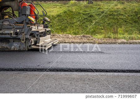 Industrial asphalt paver machine laying fresh asphalt on road construction site. Industrial asphalt paver machine laying fresh asphalt on road construction site. 71999607