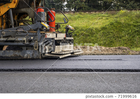 Industrial asphalt paver machine laying fresh asphalt on road construction site. Industrial asphalt paver machine laying fresh asphalt on road construction site. 71999616