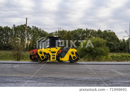 Asphalt road roller with heavy vibration roller compactor press new hot asphalt on the roadway on a road construction site. Heavy Vibration roller at asphalt pavement working. Repairing. Asphalt road roller with heavy vibration roller compactor press new hot asphalt on the roadway on a road construction site. Heavy Vibration roller at asphalt pavement working. Repairing. 71999691