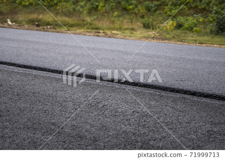 A large layer of fresh hot asphalt. Layer of asphalt raw material in a shallow depth of field. Rollers rollin fresh hot asphalt on the new road. Road construction. Construction of a new road. A large layer of fresh hot asphalt. Layer of asphalt raw material in a shallow depth of field. Rollers rollin fresh hot asphalt on the new road. Road construction. Construction of a new road. 71999713