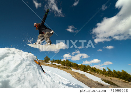 Stylish woman snowboarder makes a trick in flight. Snowboard jump from a kicker against the backdrop of mountains. Freestyle winter sports Stylish woman snowboarder makes a trick in flight. Snowboard jump from a kicker against the backdrop of mountains. Freestyle winter sports 71999928