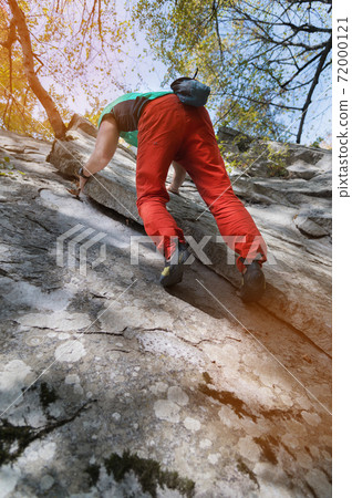 An adult bearded man in the age is practicing rock climbing on a home spot a large rock in the forest in a sunny day 72000121