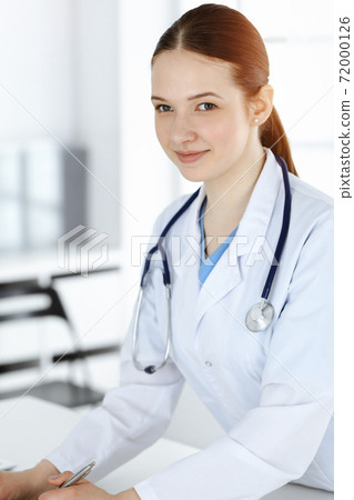 Woman-doctor at work. Female physician or internal student filling up medical documents or prescription while standing in clinic reception desk. Data in medicine Woman-doctor at work. Female physician or internal student filling up medical documents or prescription while standing in clinic reception desk. Data in medicine 72000126