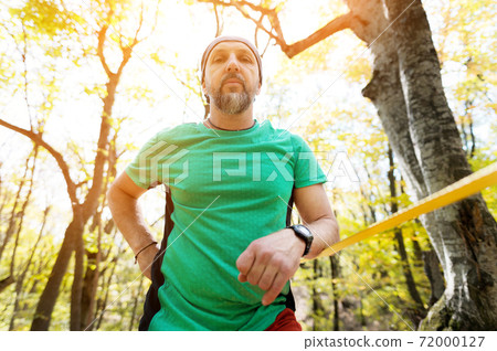 Portrait of a bearded man in age stands near a taut slackline in an autumn forest Portrait of a bearded man in age stands near a taut slackline in an autumn forest 72000127