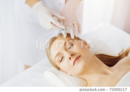 Beautician doctor doing beauty procedure with syringe to caucasian female face in synny room. Cosmetic medicine and surgery, beauty injections concept Beautician doctor doing beauty procedure with syringe to caucasian female face in synny room. Cosmetic medicine and surgery, beauty injections concept 72000217