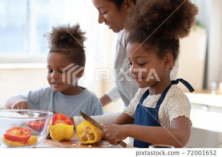 Smiling black foster mother watching adopted children cooking vegetable dish Smiling black foster mother watching adopted children cooking vegetable dish 72001652