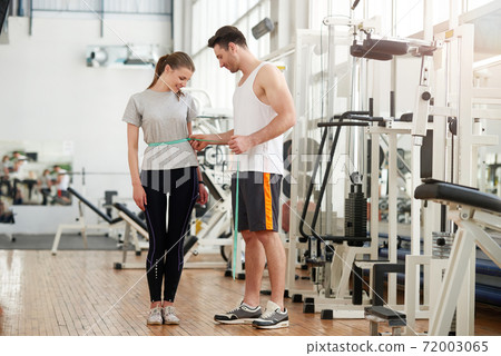 Personal trainer measuring a woman waist at the fitness club. Personal trainer measuring a woman waist at the fitness club. 72003065