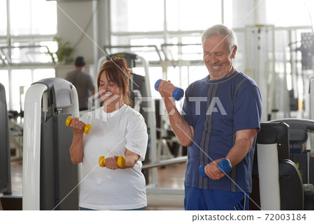 Happy senior couple lifting dumbbells at gym. Happy senior couple lifting dumbbells at gym. 72003184